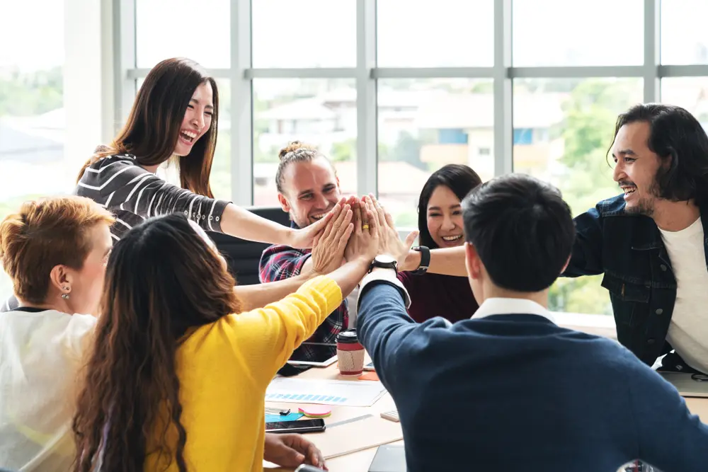 Hybrid corporate team in India engaging in a virtual team building activity — some employees in office, others joining remotely on laptops